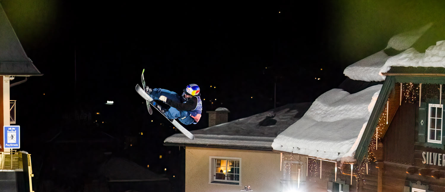 Skifahrer macht Trick in der Luft vor Häusern und dem Nachthimmel