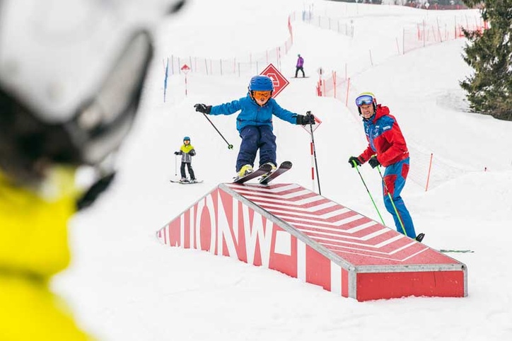 Kind springt über rotes Obstacle mit Zuschauern