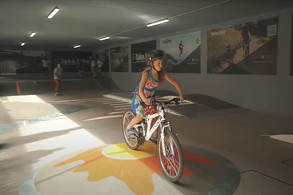 Mädchen fährt mit Fahrrad über ein flaches Rollspielelement in einer Halle
