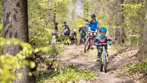 Kind fährt auf einfachem Trail vor Eltern durch Herbstwald