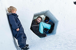 Mädchen versteckt sich in einem Schneeloch vor kleinem Jungen
