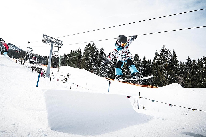 Child jumps with snowboard in kids slopestyle Nesselwang