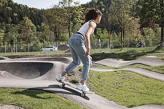 Mädchen fährt mit Skateboard auf Pumptrack bergab